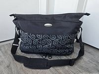 Front view showing gray swirl front panel, logo badge, strap and padded shoulder pad