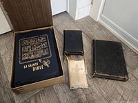 Four bibles arranged on floor including boxed French bible, small black bible, lace-trimmed testament, worn black bible