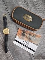 Watch, storage case, paperwork displayed on wood surface