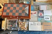 Top view showing wooden compendium with chess board lid, bags of chess pieces, various card decks and Tennis game