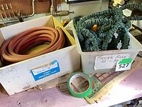 Both hoses in their containers: red-orange rubber hose in cardboard box, green expandable hose in plastic bin