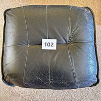top view of black faux leather ottoman showing wear and stitched panels