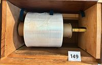 Front view of full roll of clear plastic wrap on cardboard core mounted in wooden dispenser