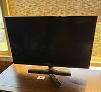 Front view of Samsung 32" LED TV on stand with remote visible