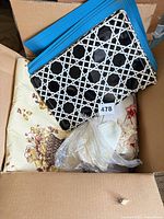 Box view showing blue placemats, black/white placemats, cream floral tablecloth and lace items