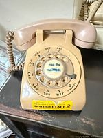 Beige Bell System rotary dial phone front view showing dial, handset, cord and sticker