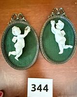 Both oval cherub plaques side by side on tabletop