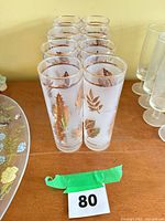 Eight frosted Collins glasses with gold leaf pattern lined in two rows