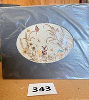 Front view of oval-matted pressed flower and paper collage artwork in protective wrap