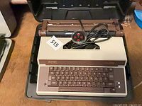 Typewriter inside open carrying case with power cord visible