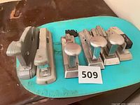 Group of six staplers on turquoise board