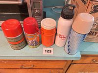 Five assorted thermoses lined up on countertop