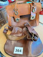 Brown leather shoulder bag and tan leather-straw satchel displayed together