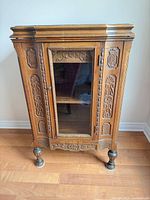 Front view of carved wood cabinet showing glass door and carved panels