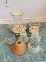 All glass items arranged together: two clear vases with sand & shells, four frosted lamp shades, one small round bowl