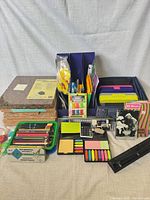 Overall lot view showing coloured pencils, cork boards, notebooks, calculator, sticky notes, hole punch, pencil grips, pencil cases