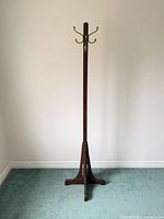 Full view of wooden coat rack standing on tripod base