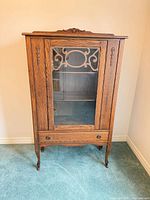 Full frontal view of oak display cabinet showing glass door, carved crest, lower drawer, cabriole legs