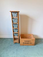 Full view of wooden shelf with five metal bins beside Tuckey Beverages crate