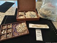 Overview showing wooden box, tray with earrings and necklaces, plastic bag of loose jewelry, boxed seed bead necklace