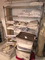Shelving with folded curtain panels, packaged curtain rods beneath, stacked plastic totes
