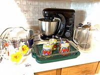 Overview showing stand mixer, saucepan, glasses carrier, condiment jars in baking dish and French press