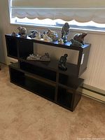 Front view of stacked black tiered shelving with sculptures on top for scale