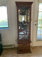 Front view of full curio cabinet showing wood finish, glass door, interior shelves, lower drawer
