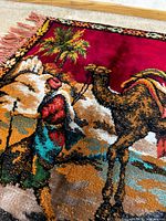 close view of camel, rider and palm tree on red field showing pile texture