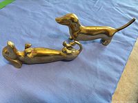 Both brass dachshund figurines on blue cloth
