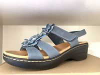 Blue sandal on box showing floral straps and wedge sole