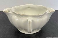 Overall view showing divided white porcelain sauce boat with central handle and twin pouring spouts