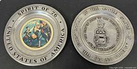 Two pewter commemorative plates side by side showing fronts