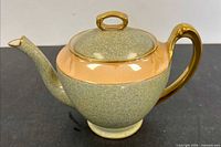 Left side view of teapot showing mottled body, peach band and gold handle