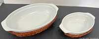 Two white stoneware roasters in matching wicker baskets