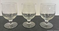 Front view of all three clear glass goblets on black surface