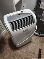 Front three-quarter view of portable air conditioner with remote on top
