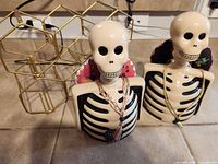 Front view of two ceramic skeleton decanters with gold honeycomb wine rack behind