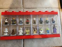 Front view of red Lego display case showing 16 minifigures in two rows