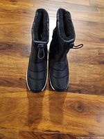 pair of black snow boots front view on wooden floor