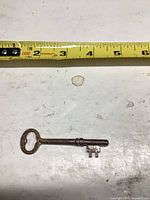 Full view of single antique skeleton key beside tape measure showing length