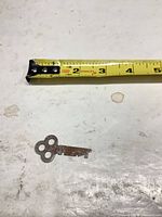 Top view of rusted skeleton key beside tape measure showing length