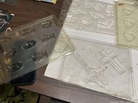 Multiple clear plastic mould sheets showing crucifix and assorted shapes