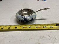 Oblique top view of porcelain bowl with metal strainer alongside tape measure