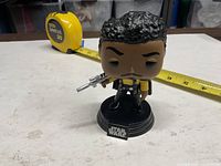 Front view of Funko Pop Lando Calrissian on base with tape measure for scale