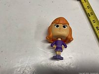 Loose Funko Pop Daphne vinyl figure shown on white surface next to tape measure