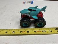 Full view of teal shark-themed Hot Wheels Monster Truck on measuring tape