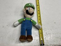 Front view of Luigi plush beside ruler showing ~11 inch length