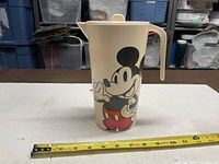 Front view of cream plastic Mickey Mouse pitcher with tape measure showing height