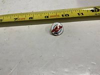 Top view of round New Jersey Devils pin beside measuring tape